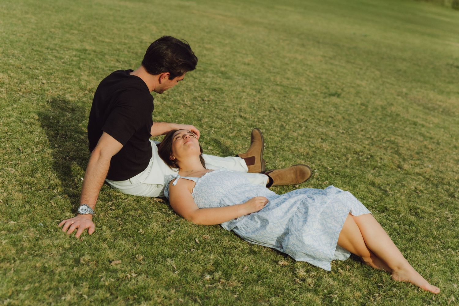 Man sitting beside woman lying on green grass during sunny outdoor photo session.