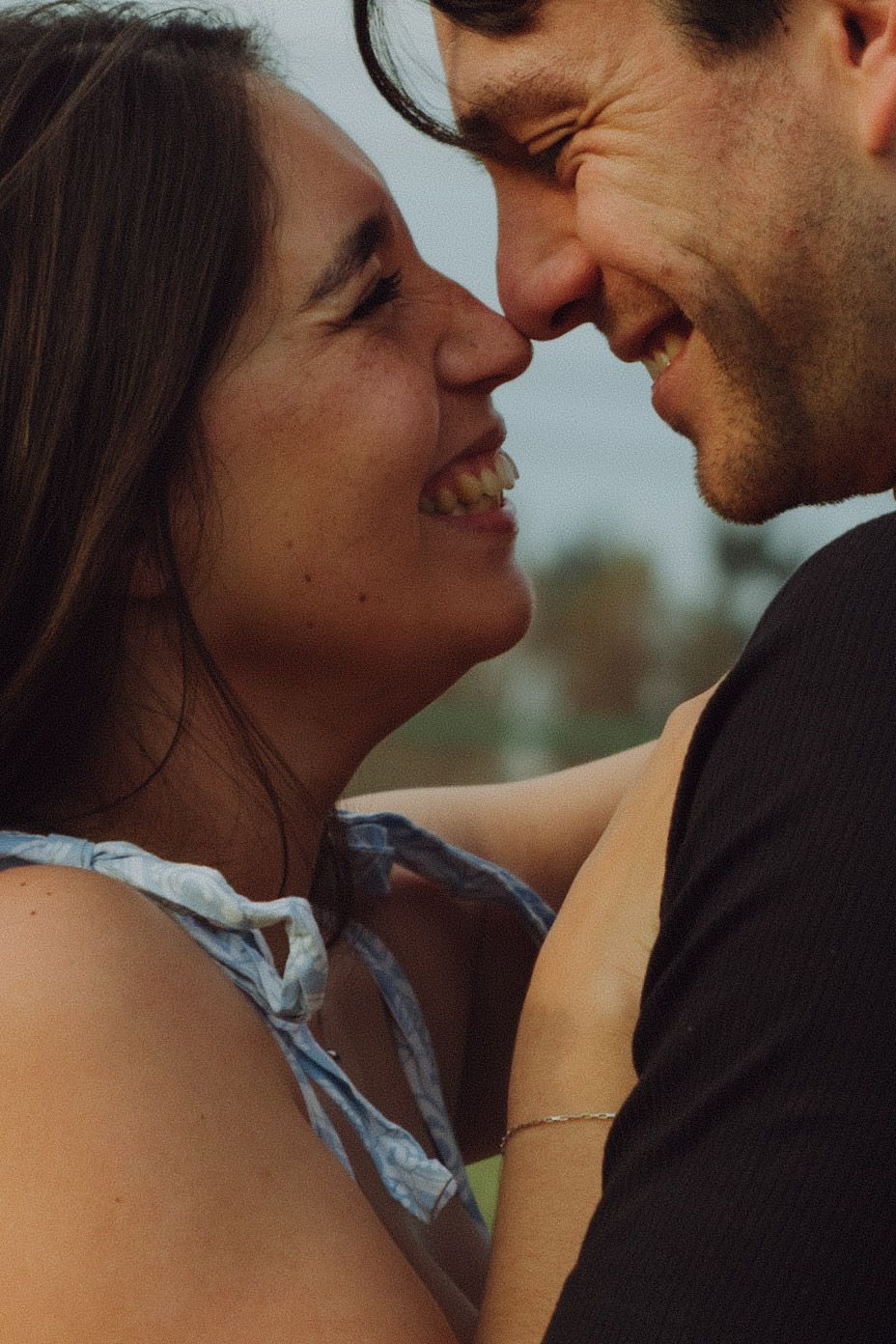 Close-up of a laughing couple touching noses in an intimate and joyful outdoor moment.
