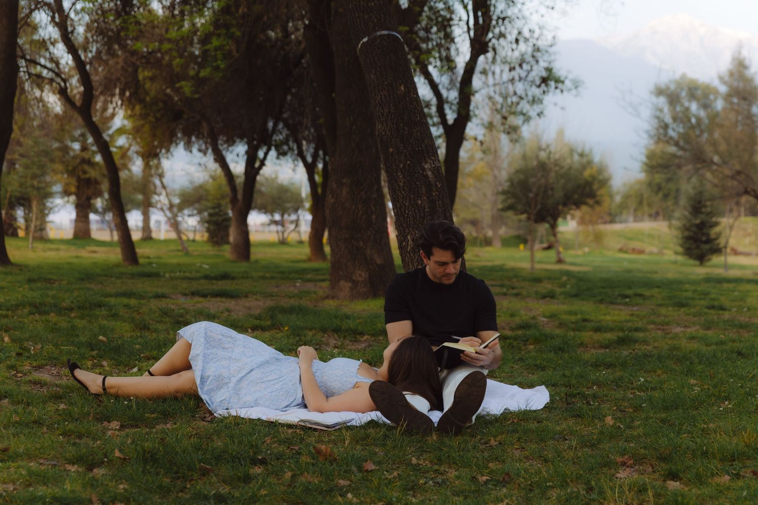 Couple relaxing in a park, woman lying on grass with head in mans lap as he reads.