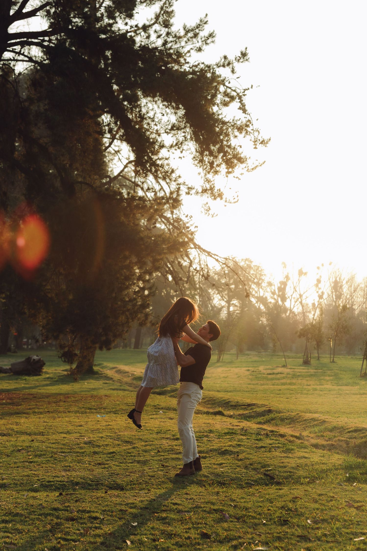 Couple sharing a romantic moment at sunset, man lifting woman in a sunlit park.