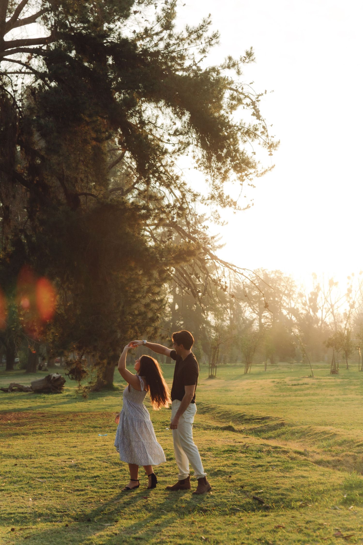 Couple dancing together in a sunlit park, woman in white dress twirling at sunset.