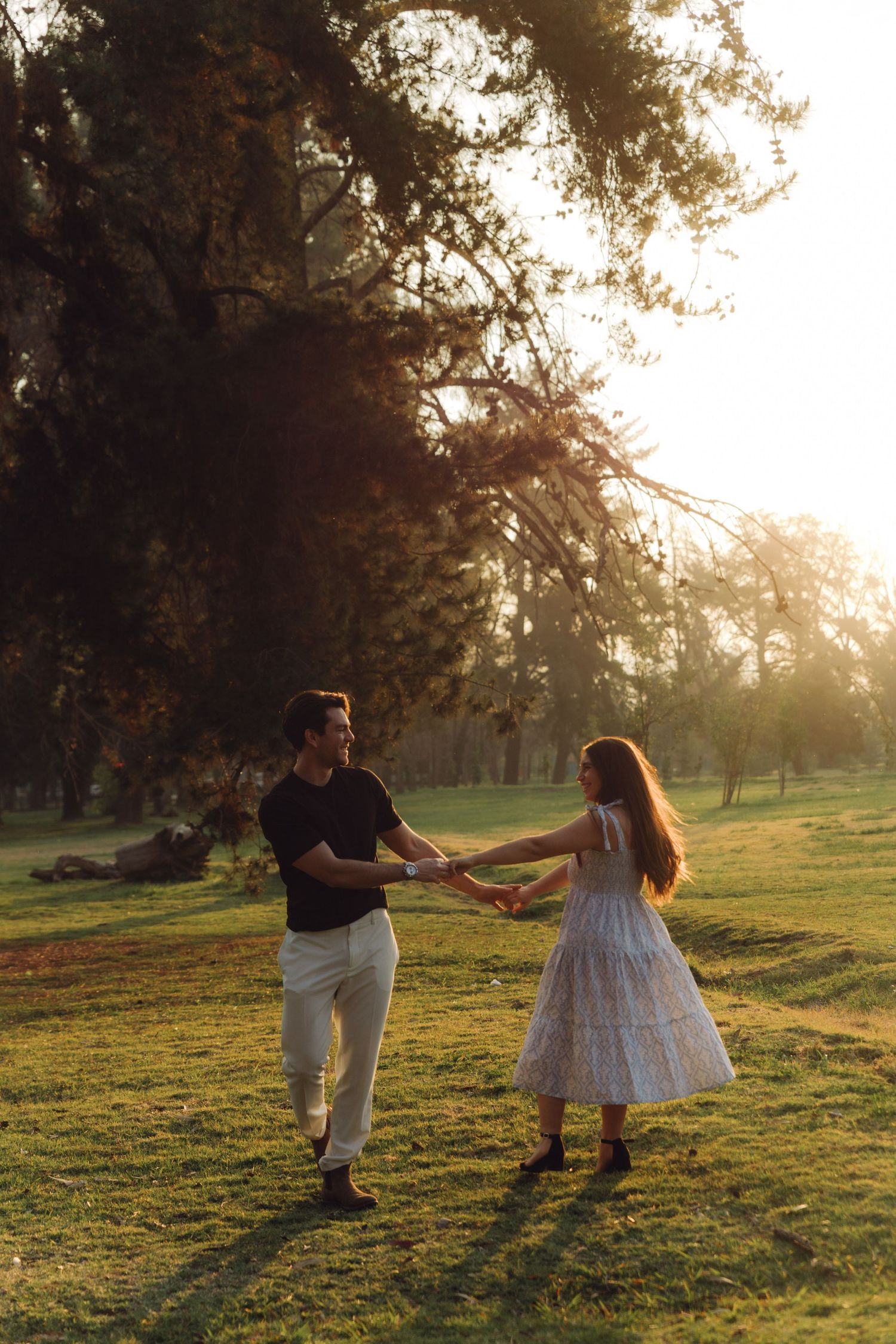 Romantic couple holding hands and dancing in a glowing golden sunset park setting.