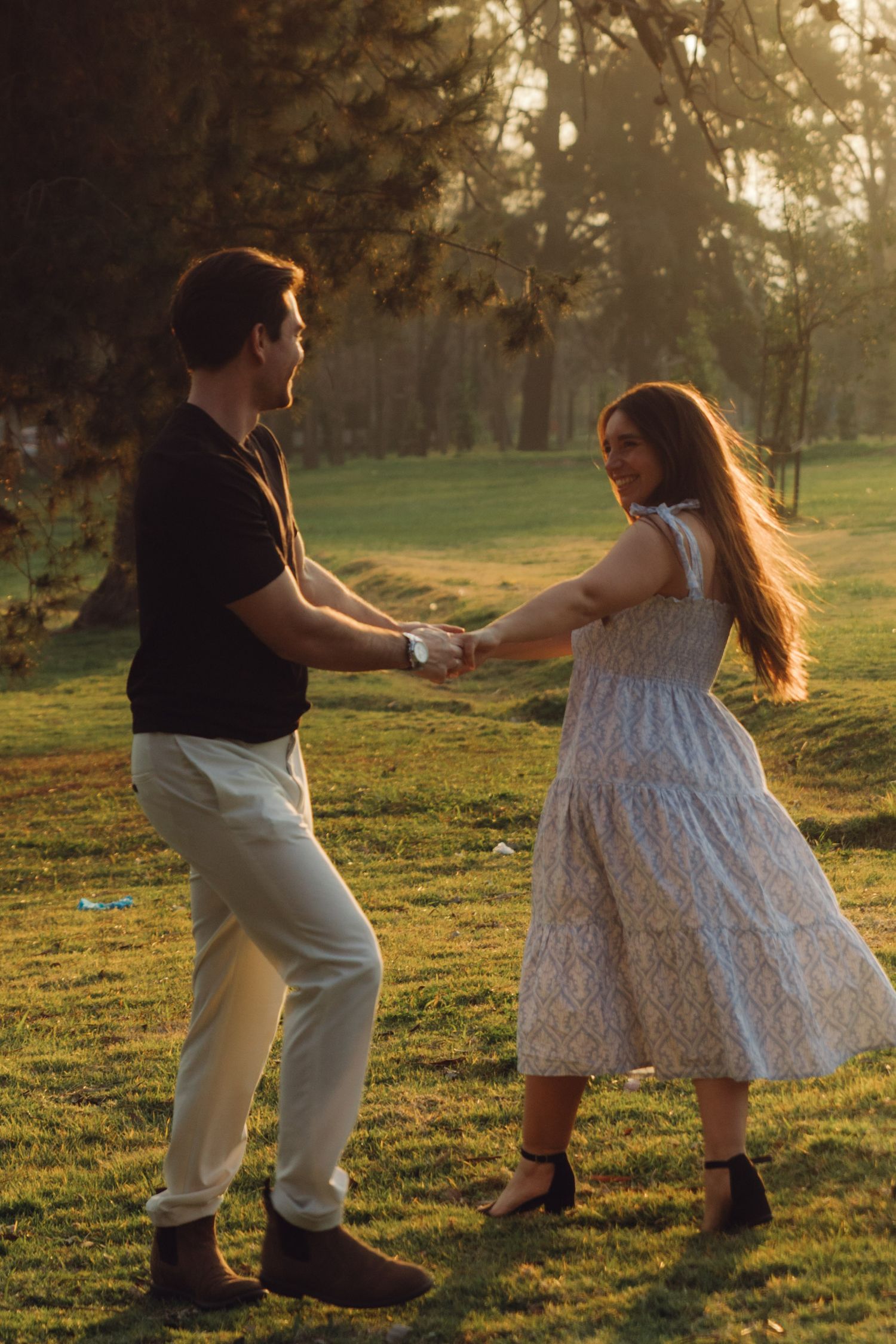 Smiling couple holding hands and dancing outdoors in warm golden sunset park light.