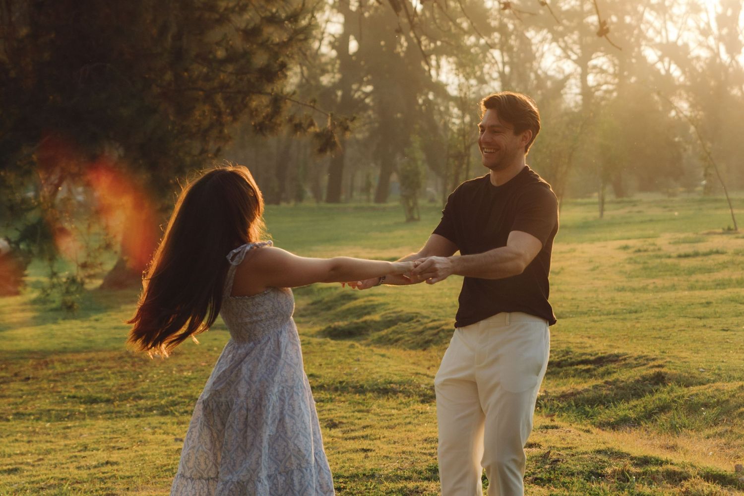 Couple spinning and holding hands in a sunny park with warm golden light.