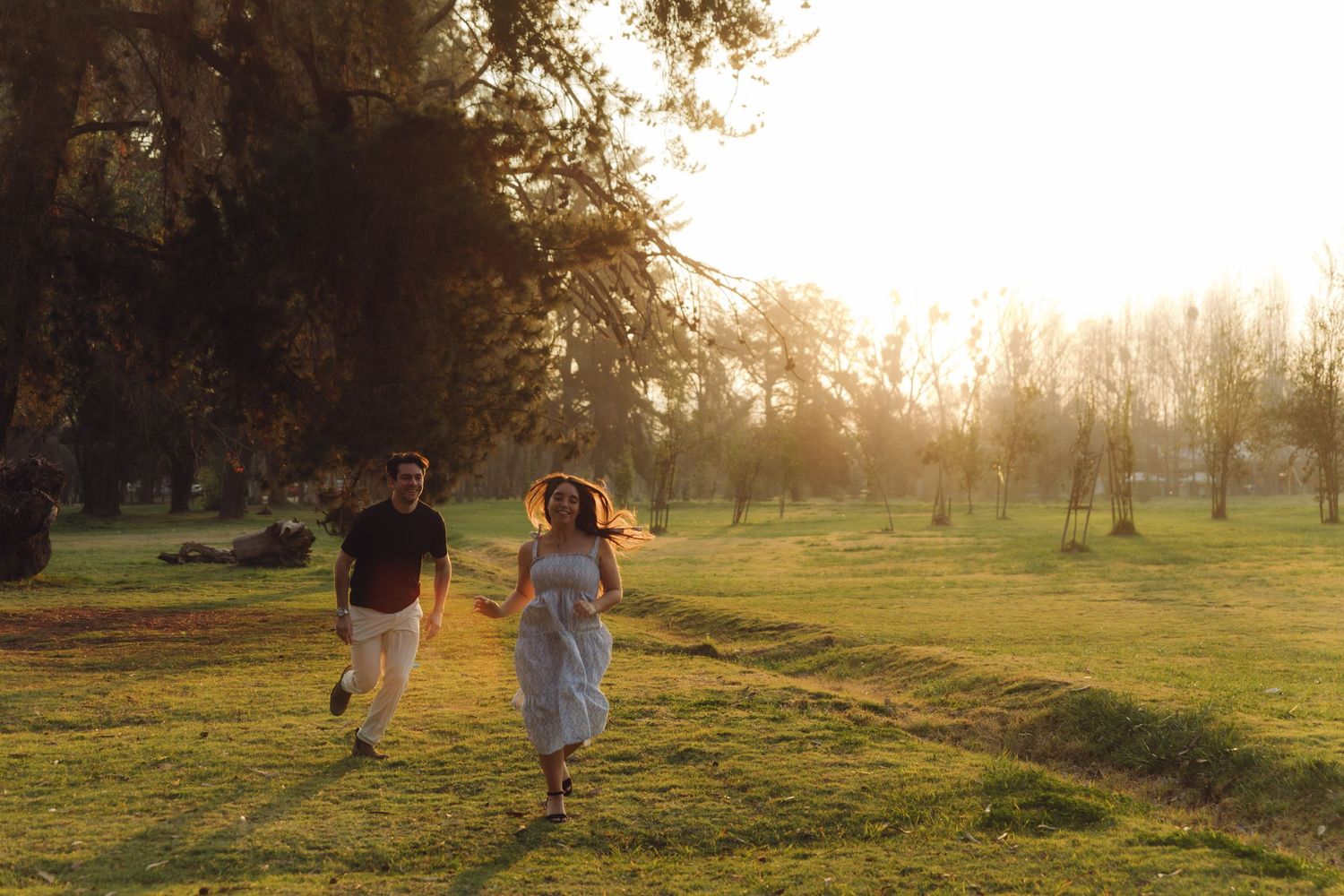 Couple running together through a beautiful golden sunlit park holding hands at dusk.