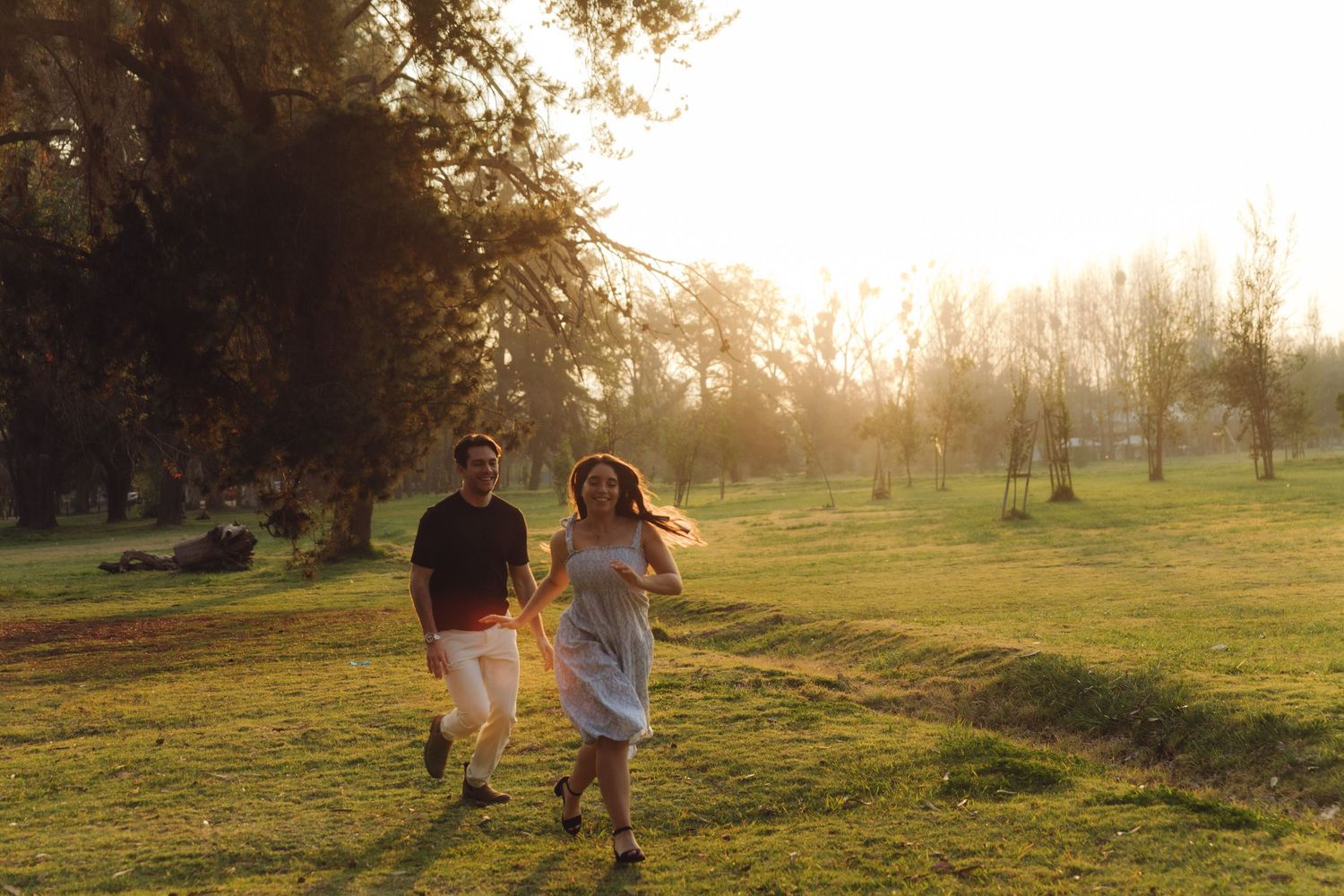Happy couple running hand in hand through a sunlit green park at sunset.