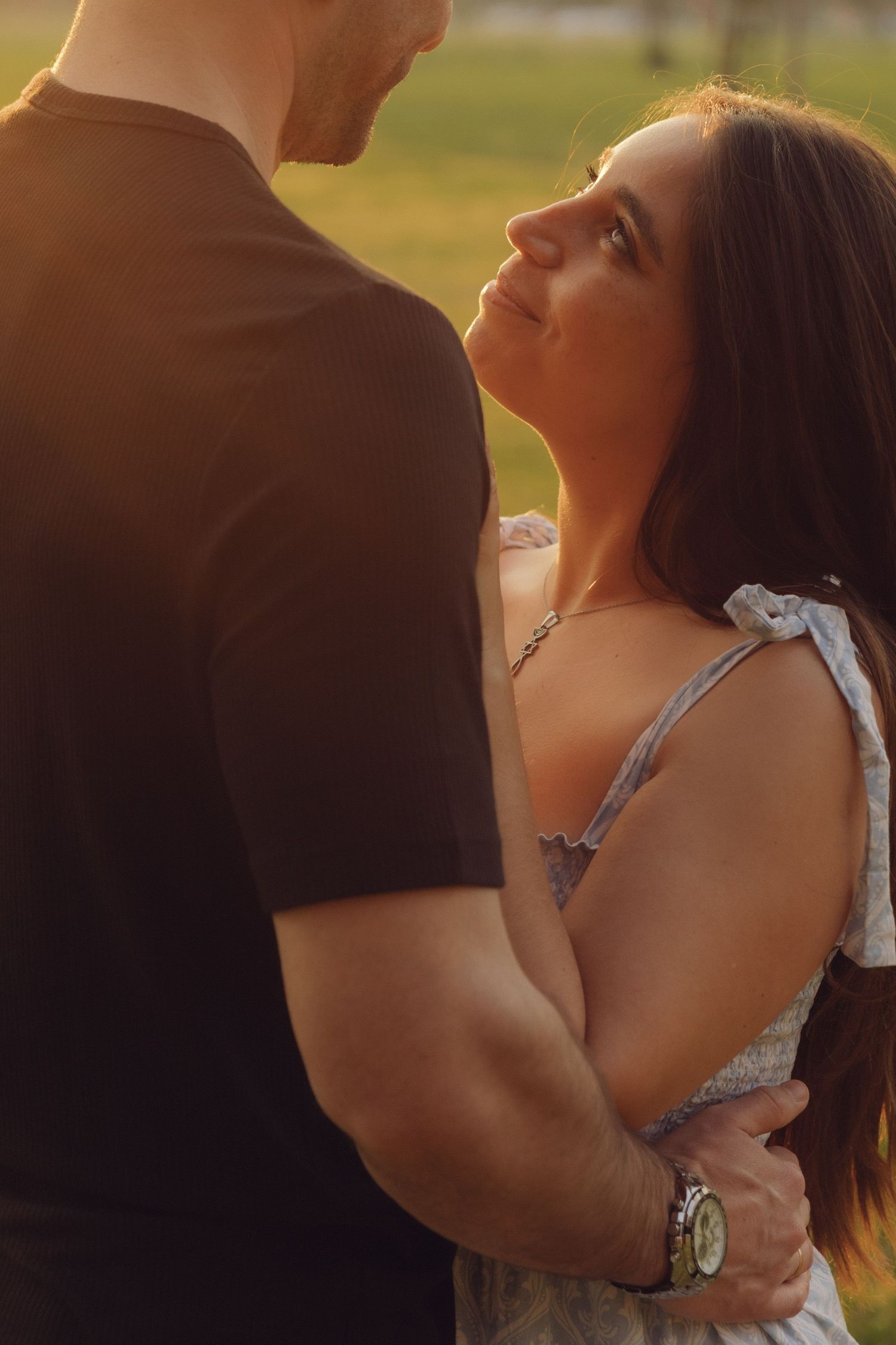 Woman in floral dress gazing up lovingly at her partner during a warm golden hour outdoor photo session.