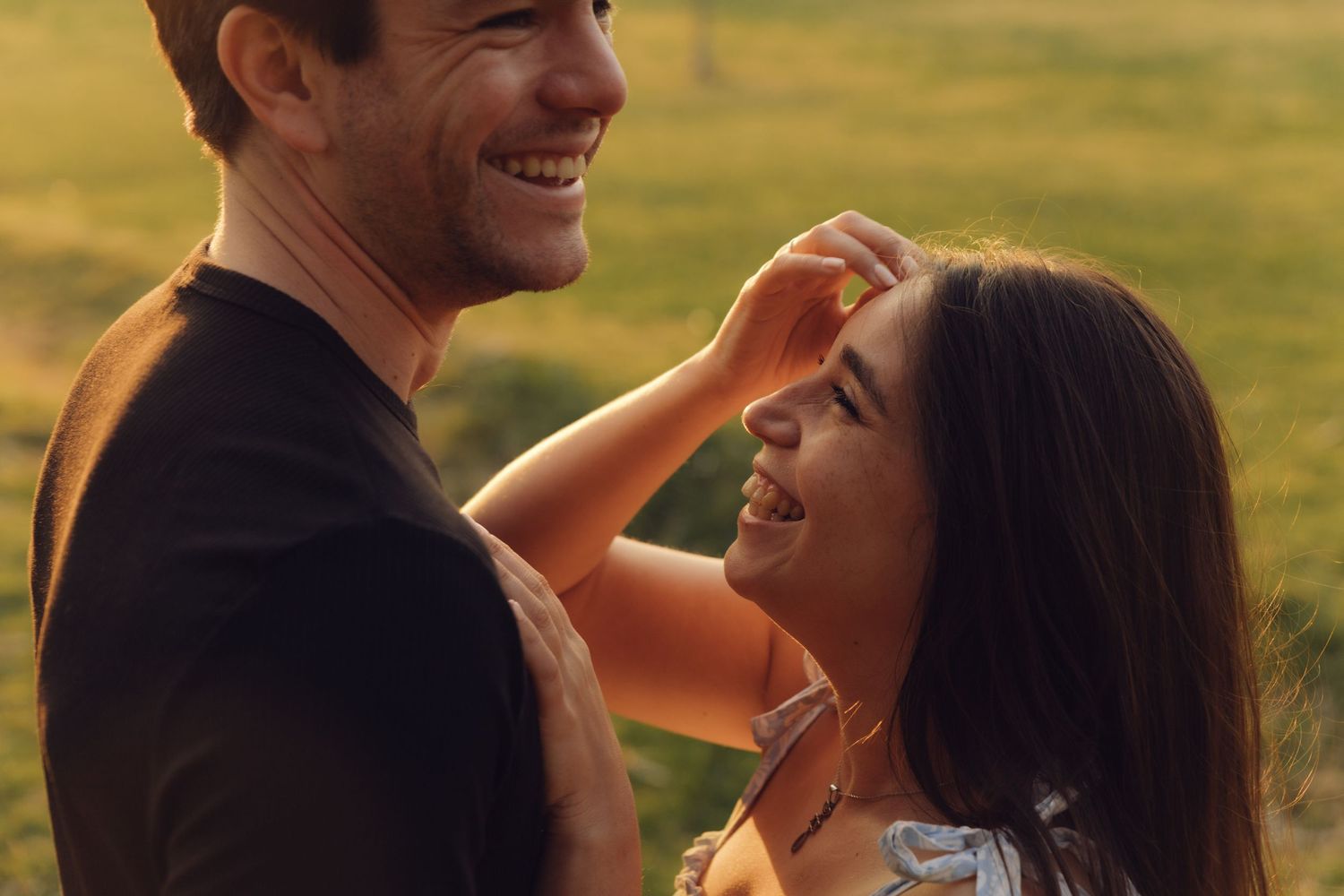 Happy couple laughing and smiling together in a sunlit field, sharing a joyful romantic moment outdoors.