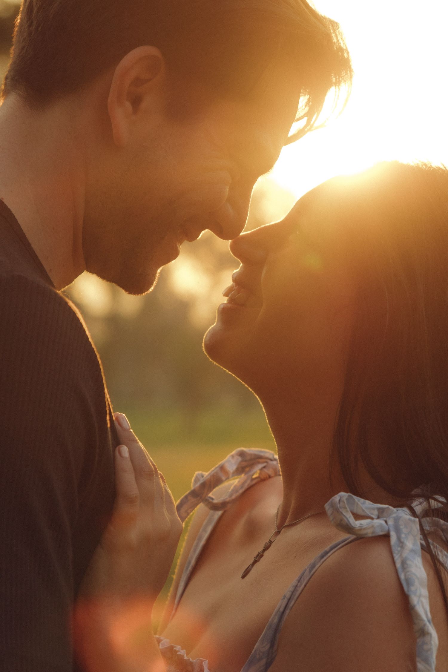 Romantic couple about to kiss with glowing sunset light behind them, faces close in an intimate moment.