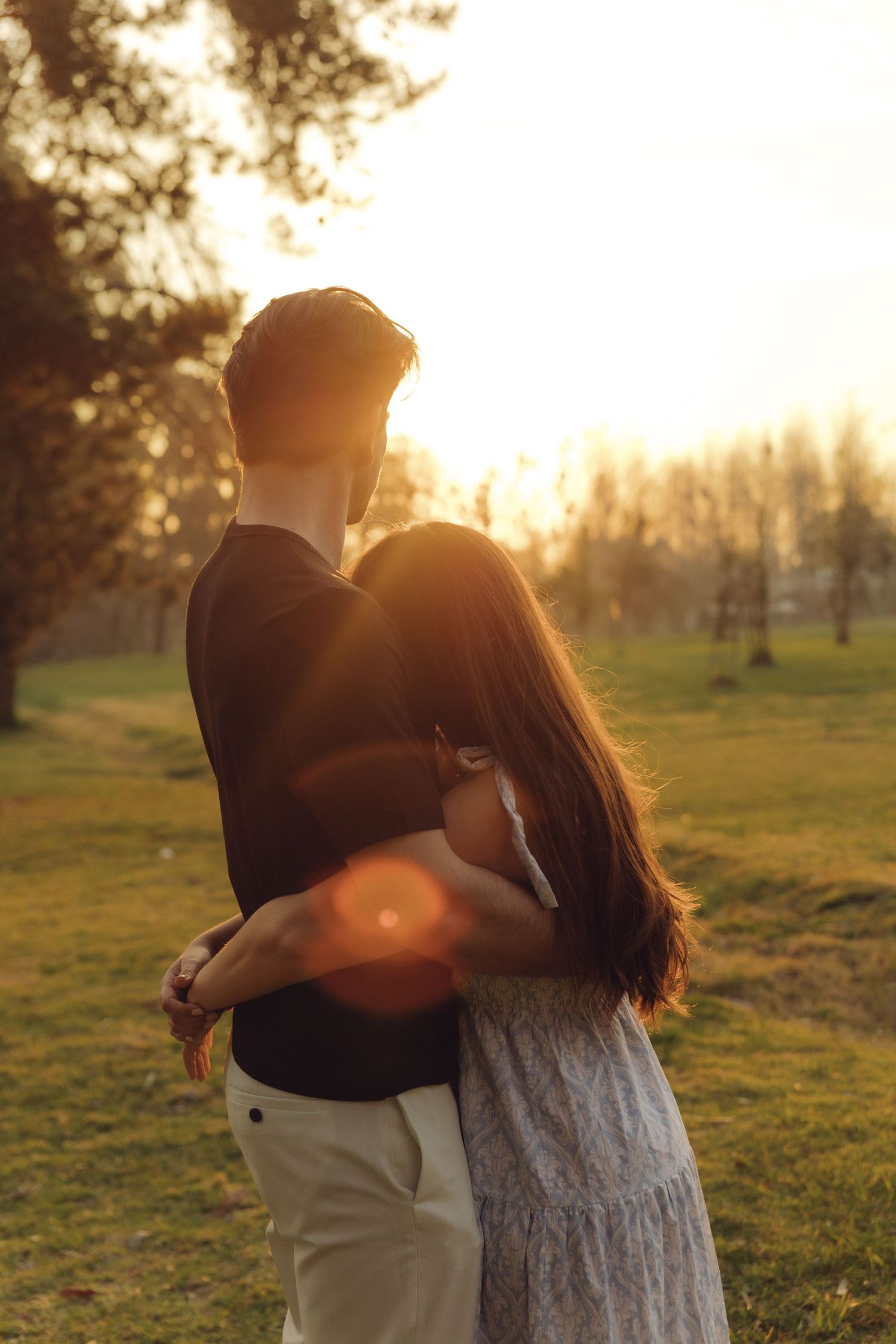 Romantic couple embracing in a park at golden sunset, backlit by warm glowing sunlight.