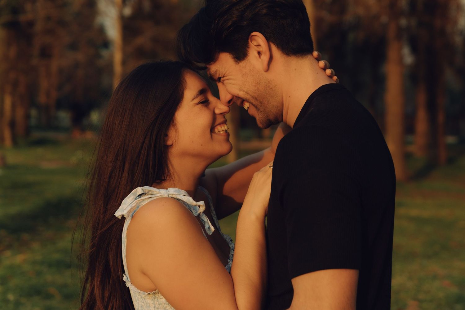 Happy couple almost kissing, smiling face to face in a warm golden park setting at dusk.