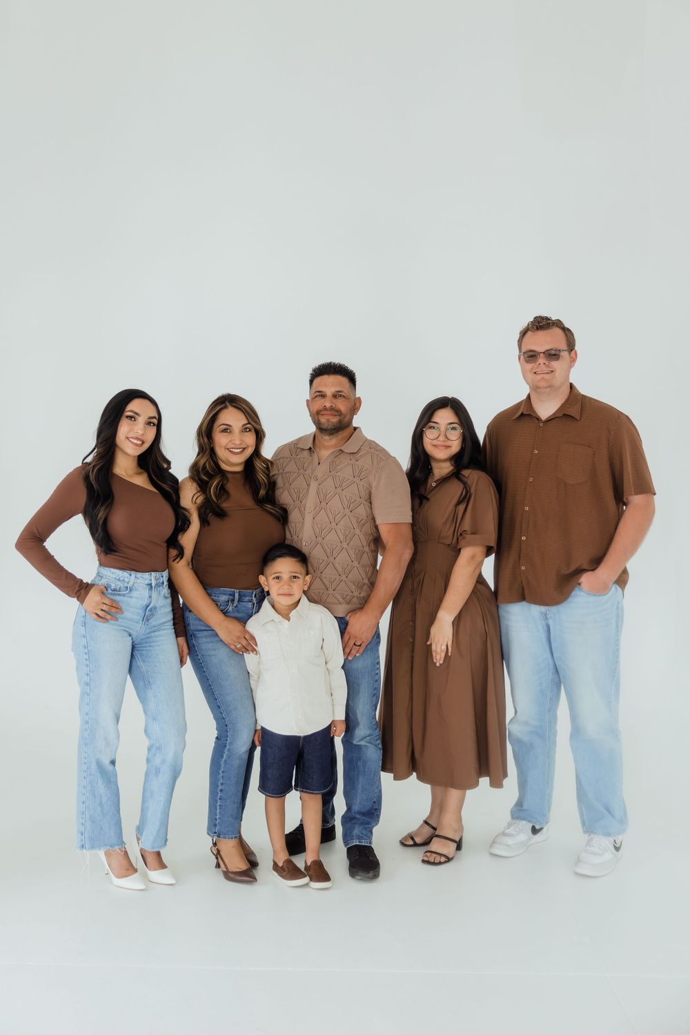 Family of six posing together in coordinating brown and denim outfits against a light gray studio background.
