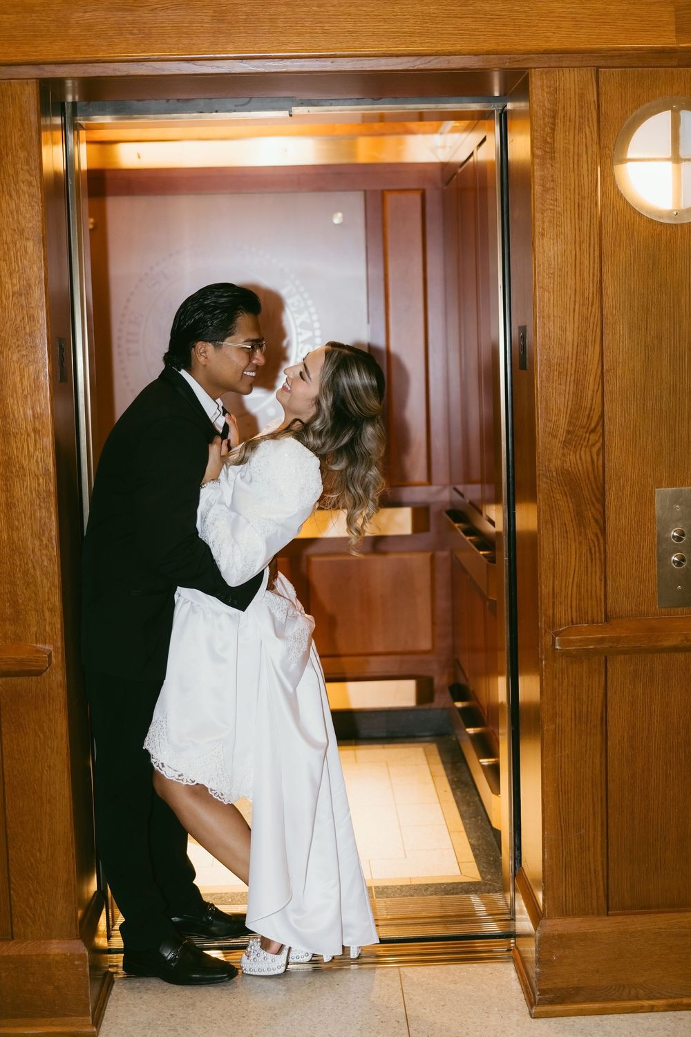 Bride and groom share a romantic embrace inside a wooden elevator, with the bride in a white gown and veil.