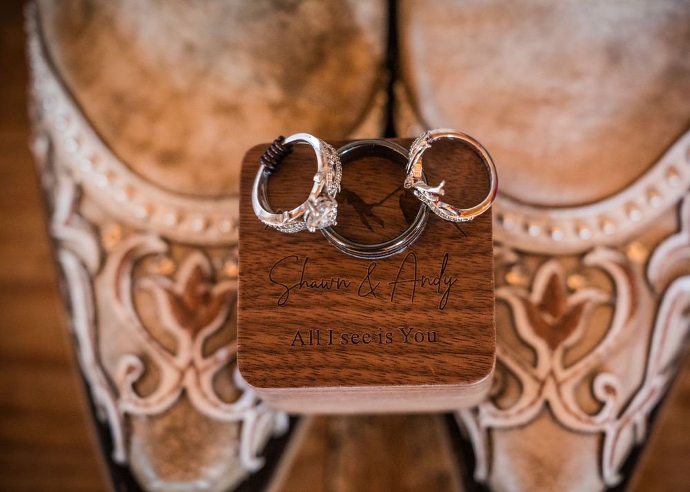 Engraved wooden wedding ring box with couples names displayed on cowboy boots.
