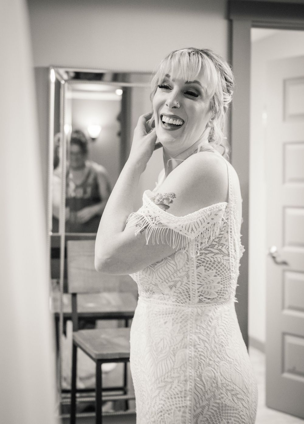 Smiling bride in lace wedding dress laughing while getting ready, black and white photo.
