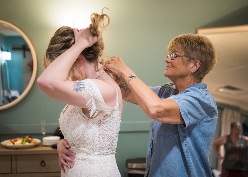 Older woman helping bride style her hair in a lace wedding dress before the ceremony.