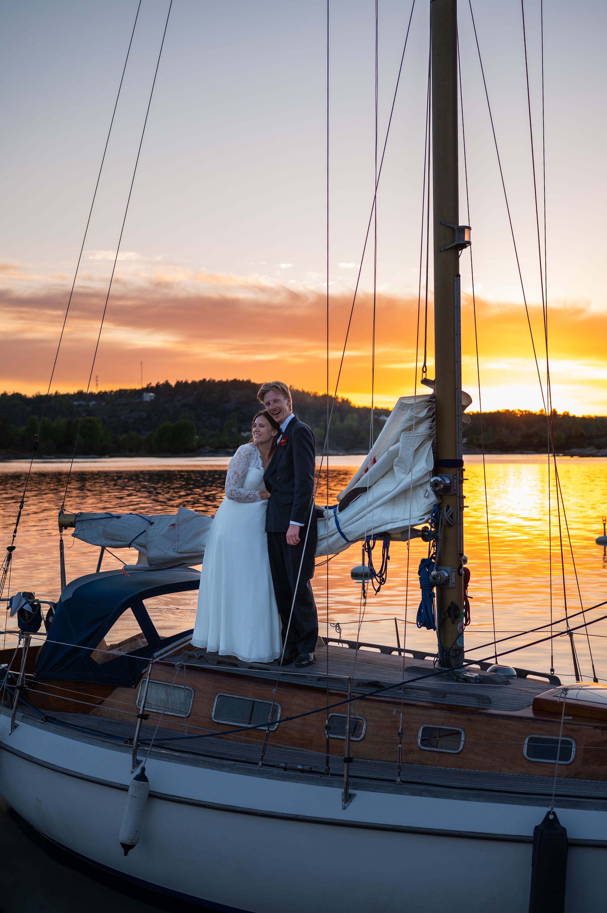 Bride and groom embracing on sailboat at golden sunset.