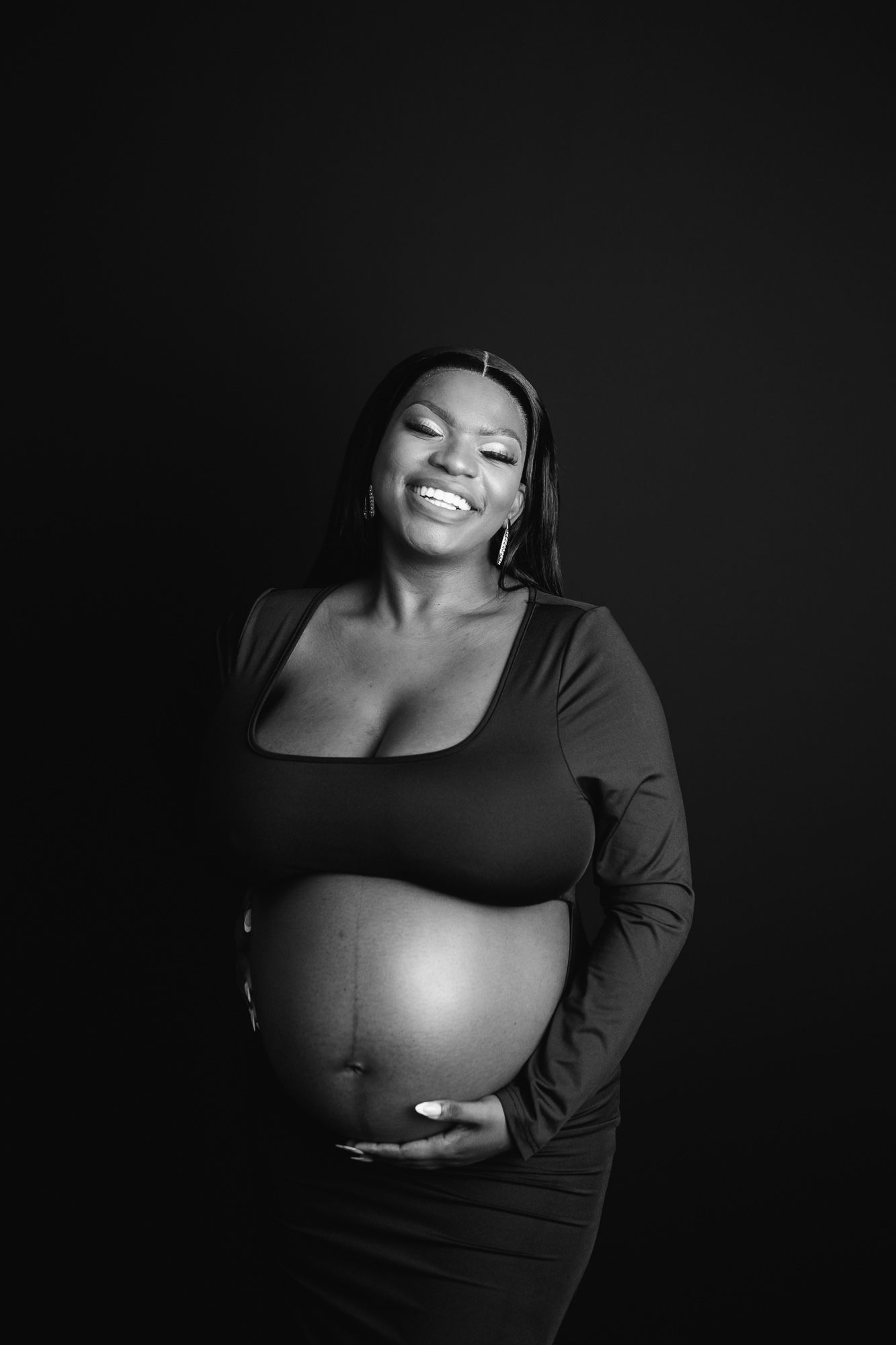 Pregnant woman smiling while holding her baby bump during studio maternity photography