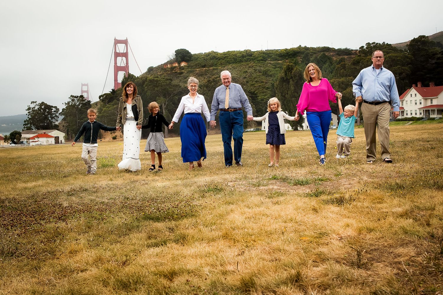 Multi-generational family holding hands walking near Golden Gate Bridge on a grassy field in San Francisco.
