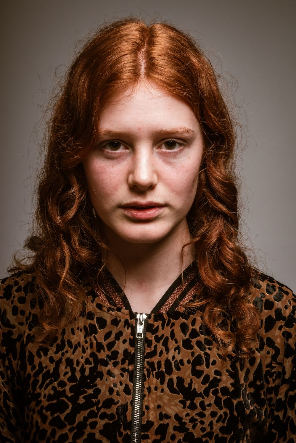 Frontaal studioportret van een jonge vrouw met lang rood krullend haar en een jas met luipaardprint bij Bart Boodts
