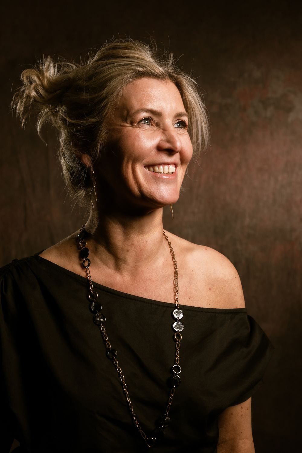 Warm belicht studioportret van een lachende vrouw, Ann Briers in een zwarte schoudervrije jurk, die opgewekt opzij kijkt bij Bart Boodts