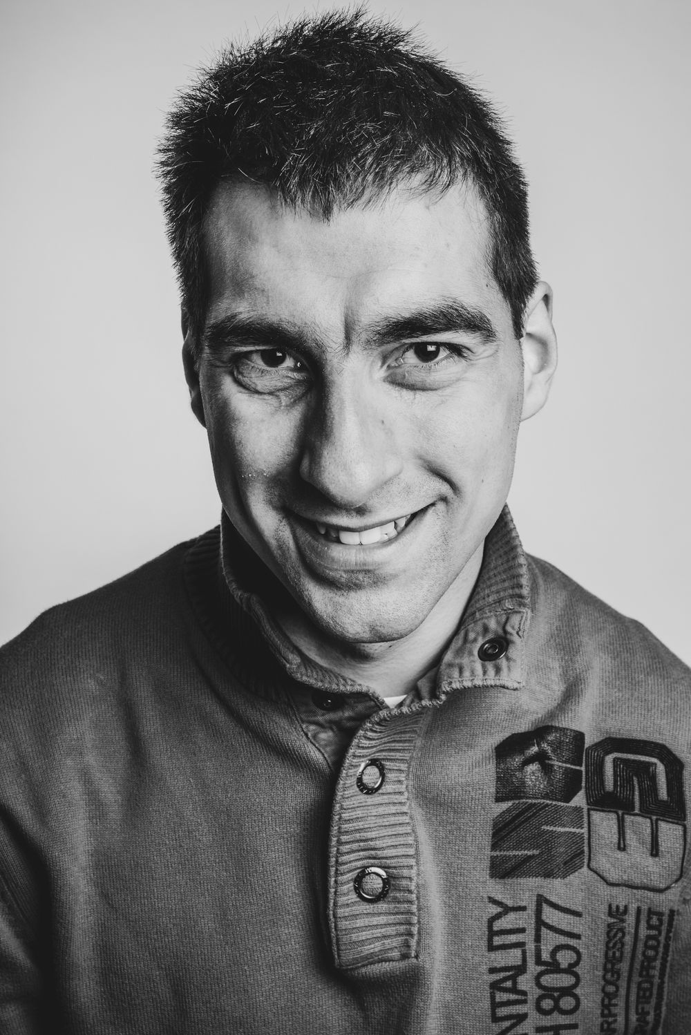 Zwart wit studioportret van een glimlachende man met kort donker haar die recht in de camera kijkt.