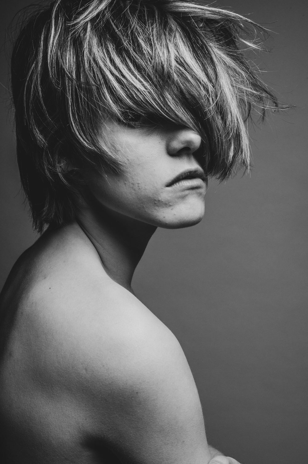 Artistiek zwart wit zijportret van een vrouw met een korte coupe die over haar ogen valt en haar schouder naar de camera draait.