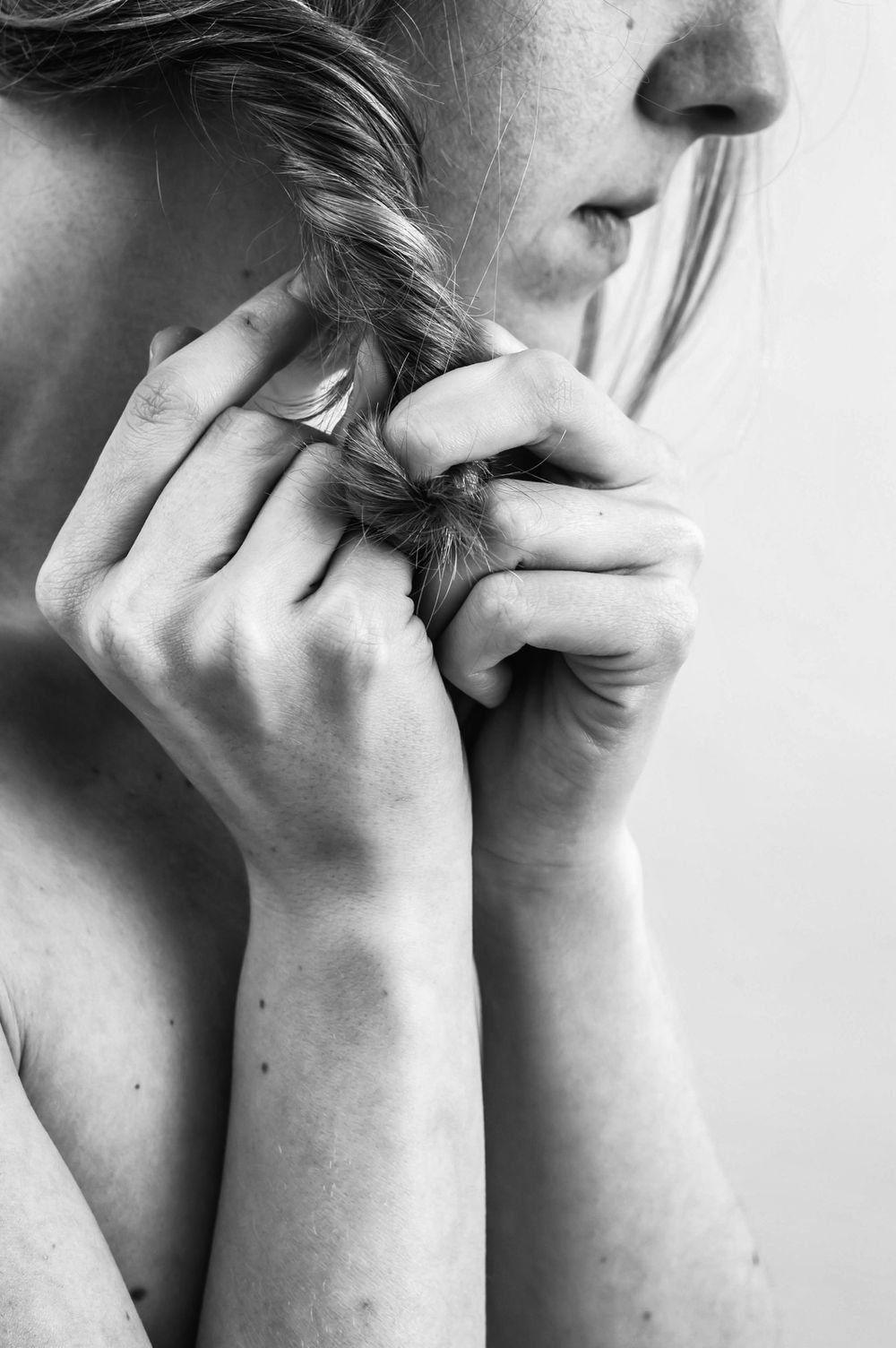 Zwart wit detailportret van een vrouw die met beide handen een vlecht bij haar gezicht vasthoudt.