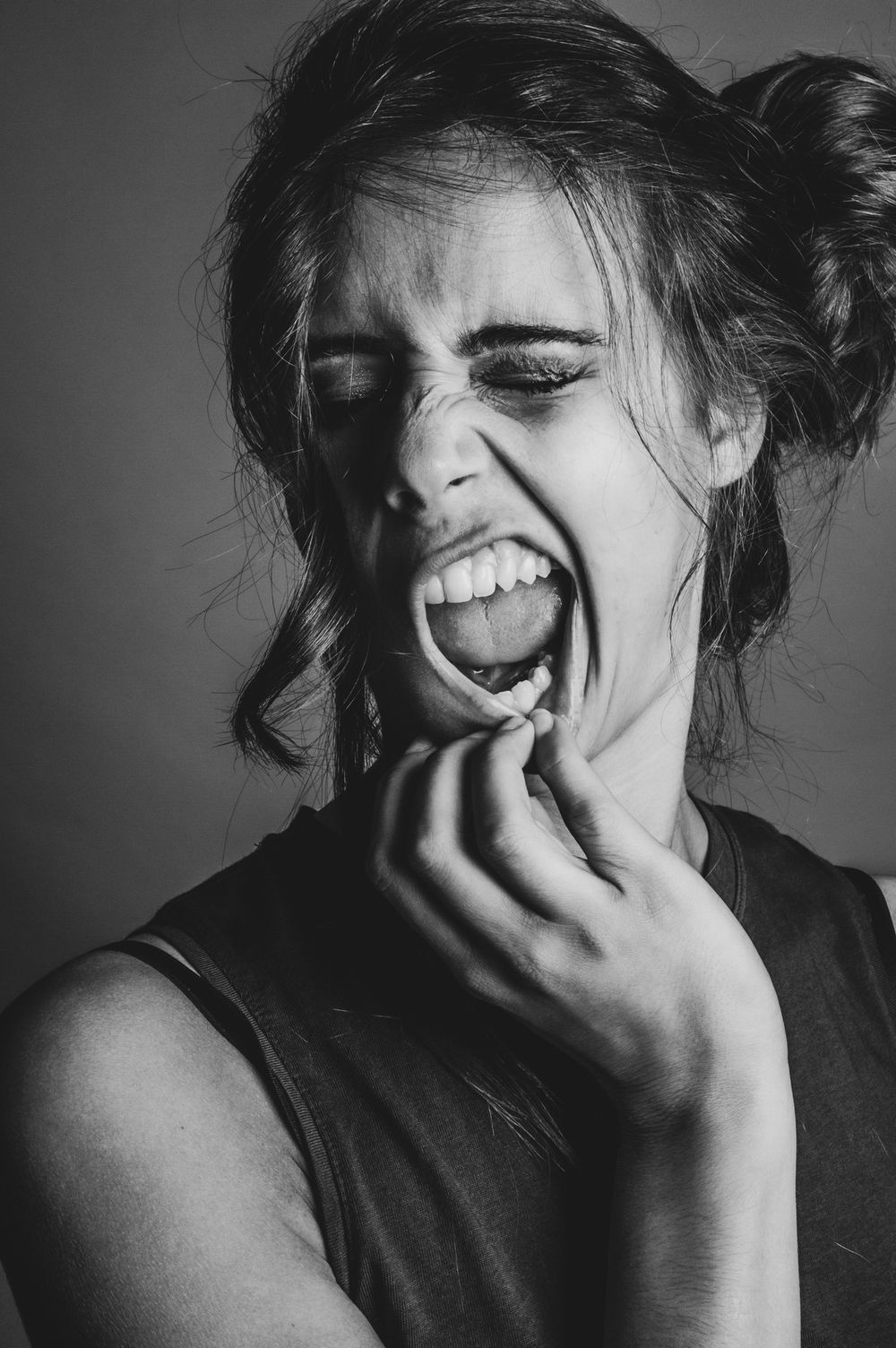 Expressief zwart wit studioportret van een vrouw met gesloten ogen en de mond wijd open, terwijl ze een hand bij haar kin houdt.