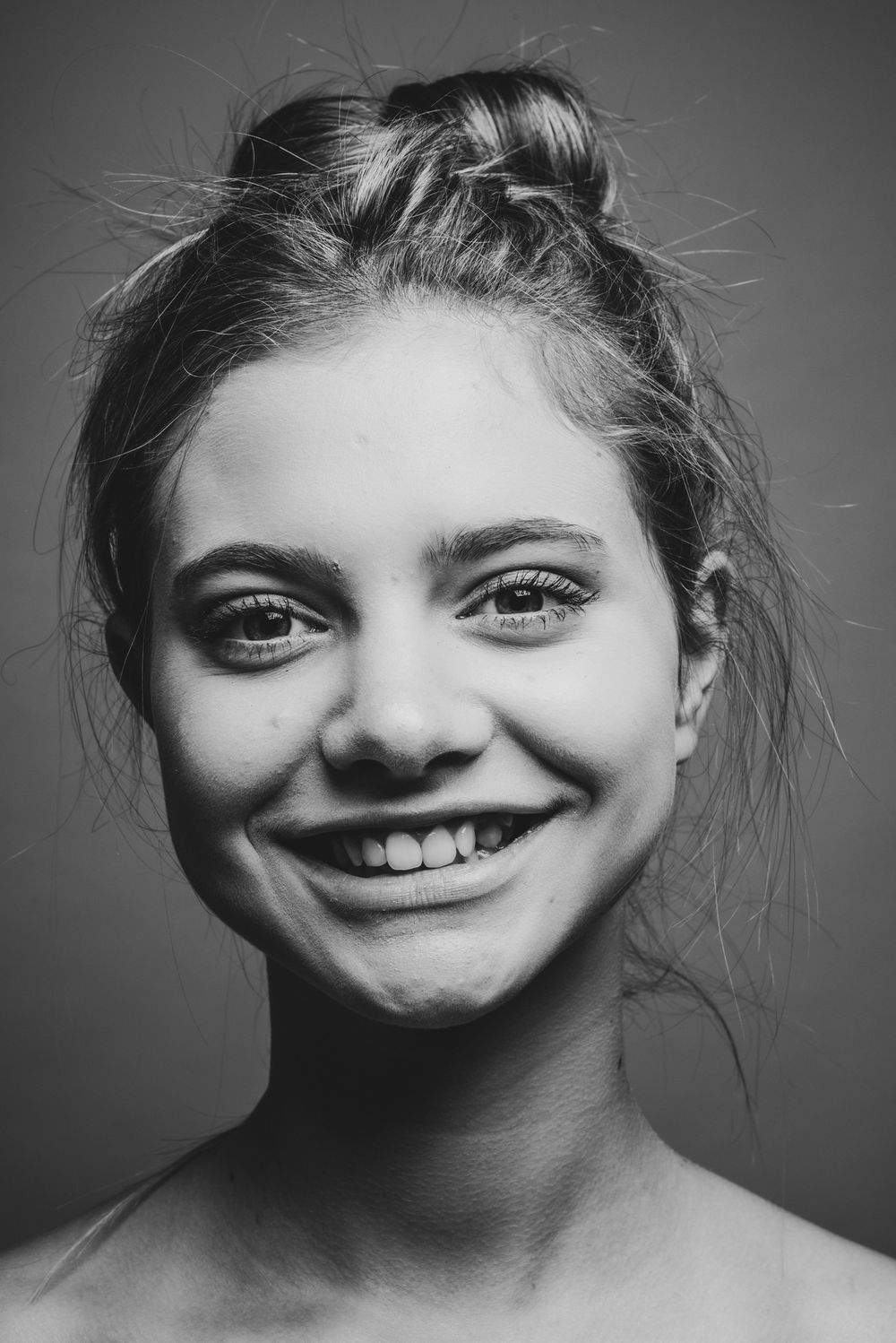 Zwart wit close portret van een glimlachende vrouw met opgestoken haar die recht in de camera kijkt.