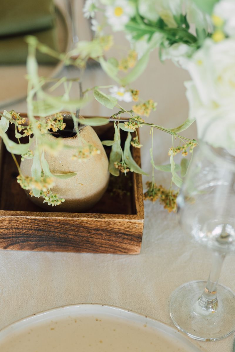 Elegant table setting with wooden box, floral stems, wine glass, and white flowers for a wedding reception.