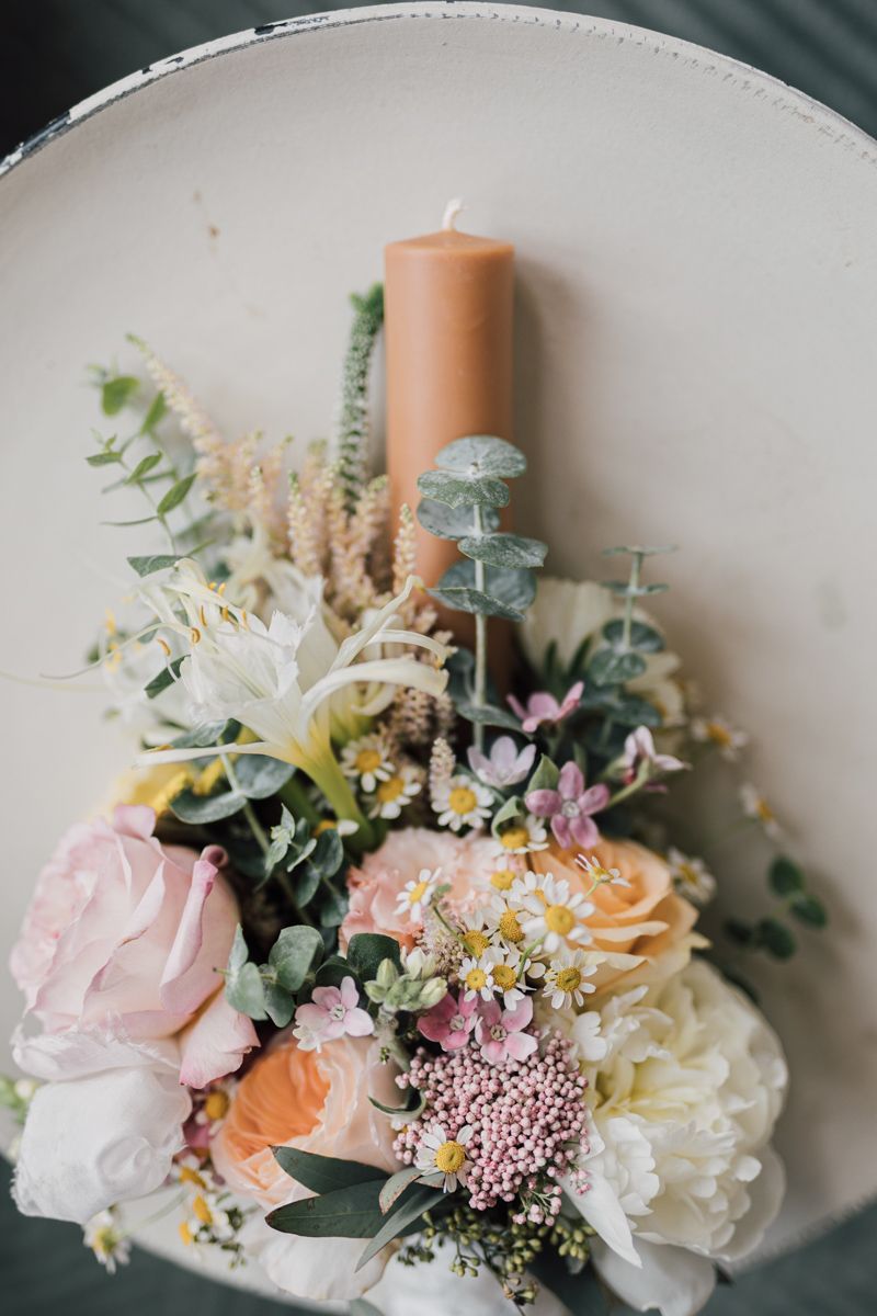 Elegant floral arrangement with pastel roses, daisies, eucalyptus, and a peach pillar candle in a vintage hat box.
