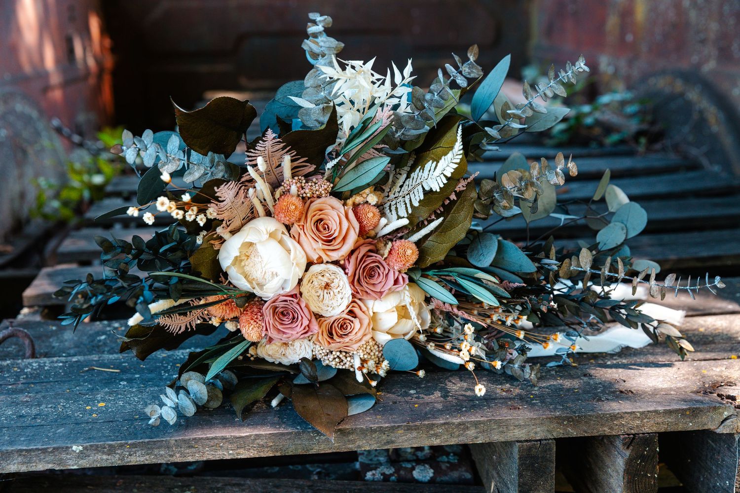 Rustic wedding bouquet with peach roses, white blooms, and eucalyptus greenery resting on weathered wood surface.