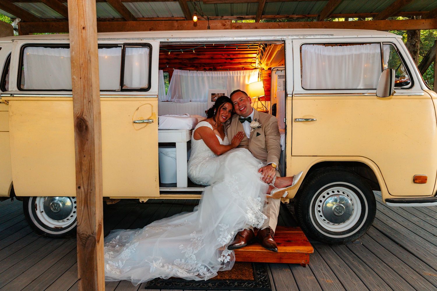 Bride and groom sitting in a vintage yellow VW camper van, sharing a romantic moment on their wedding day.
