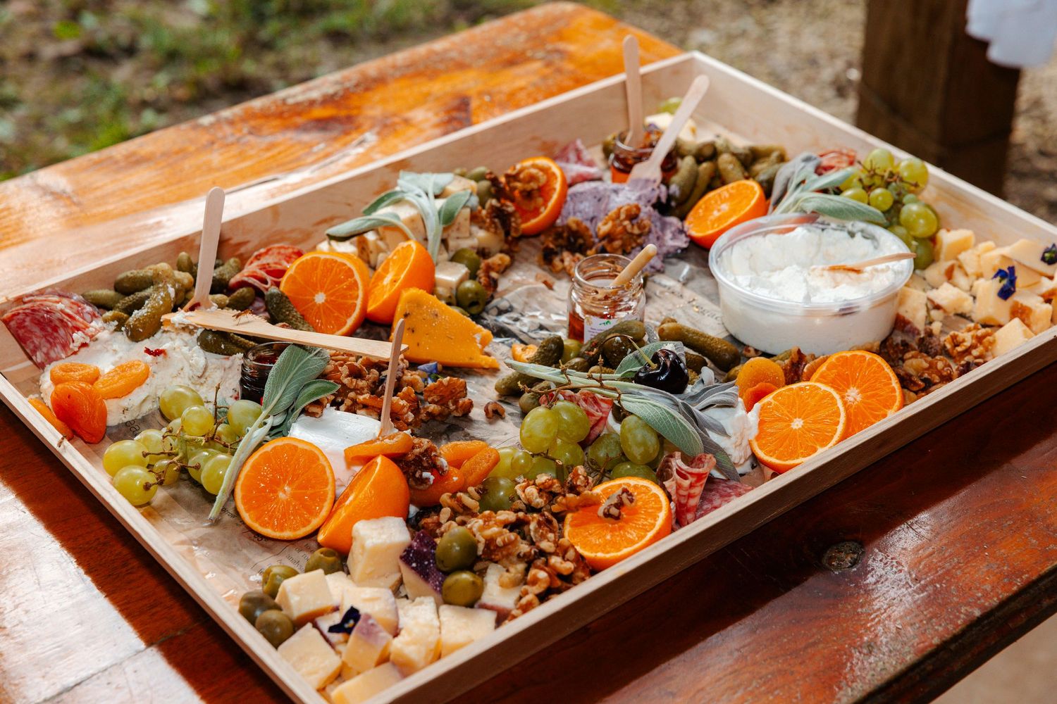 Colorful charcuterie board with fresh oranges, grapes, cheese, nuts, and dipping sauce on a wooden tray.