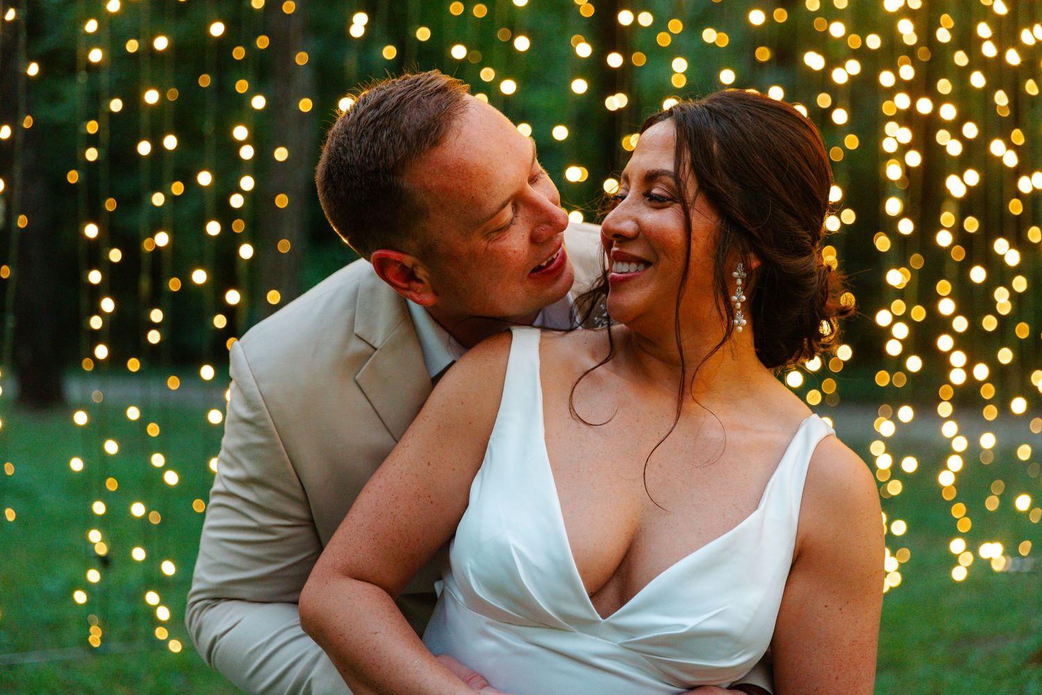 Newlyweds sharing a romantic moment surrounded by warm bokeh string lights at dusk.