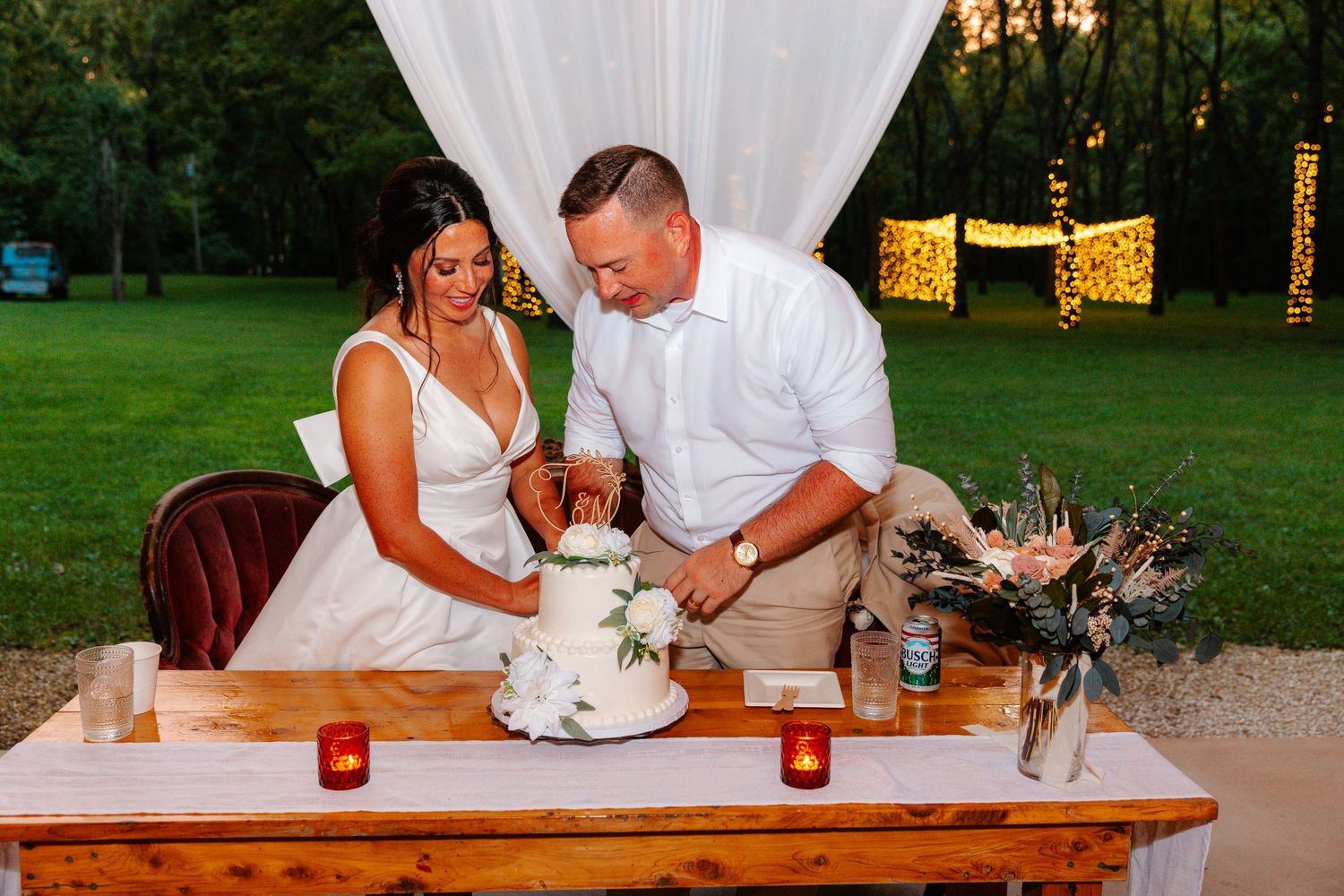 Bride and groom cutting their wedding cake at an outdoor reception table at sunset.