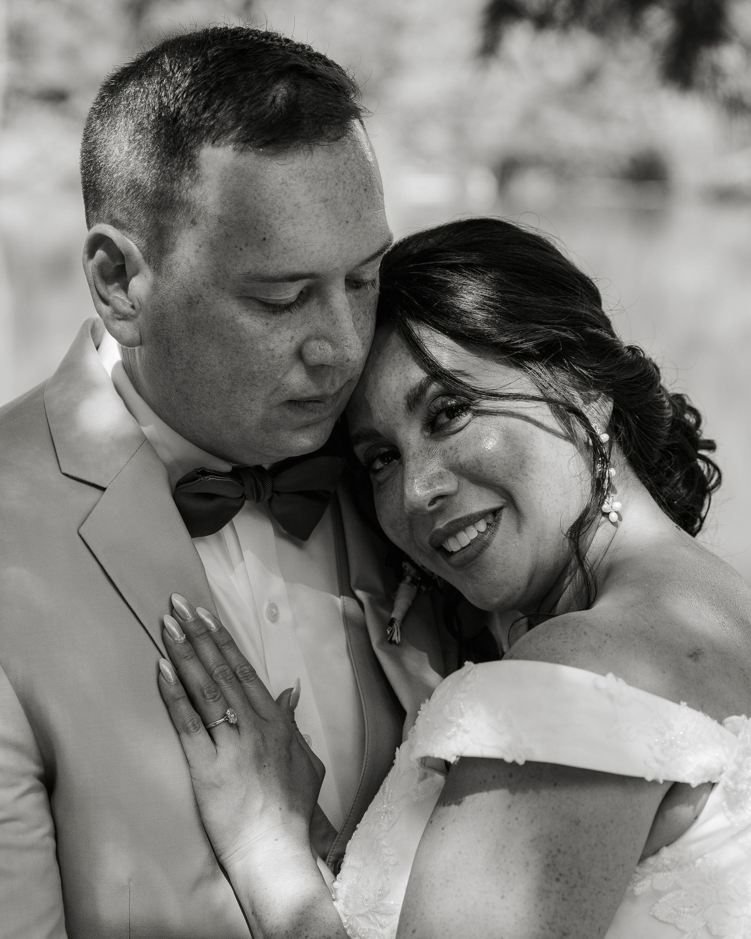 Black and white close-up of a groom in a bow tie embracing his smiling bride in an off-shoulder gown.