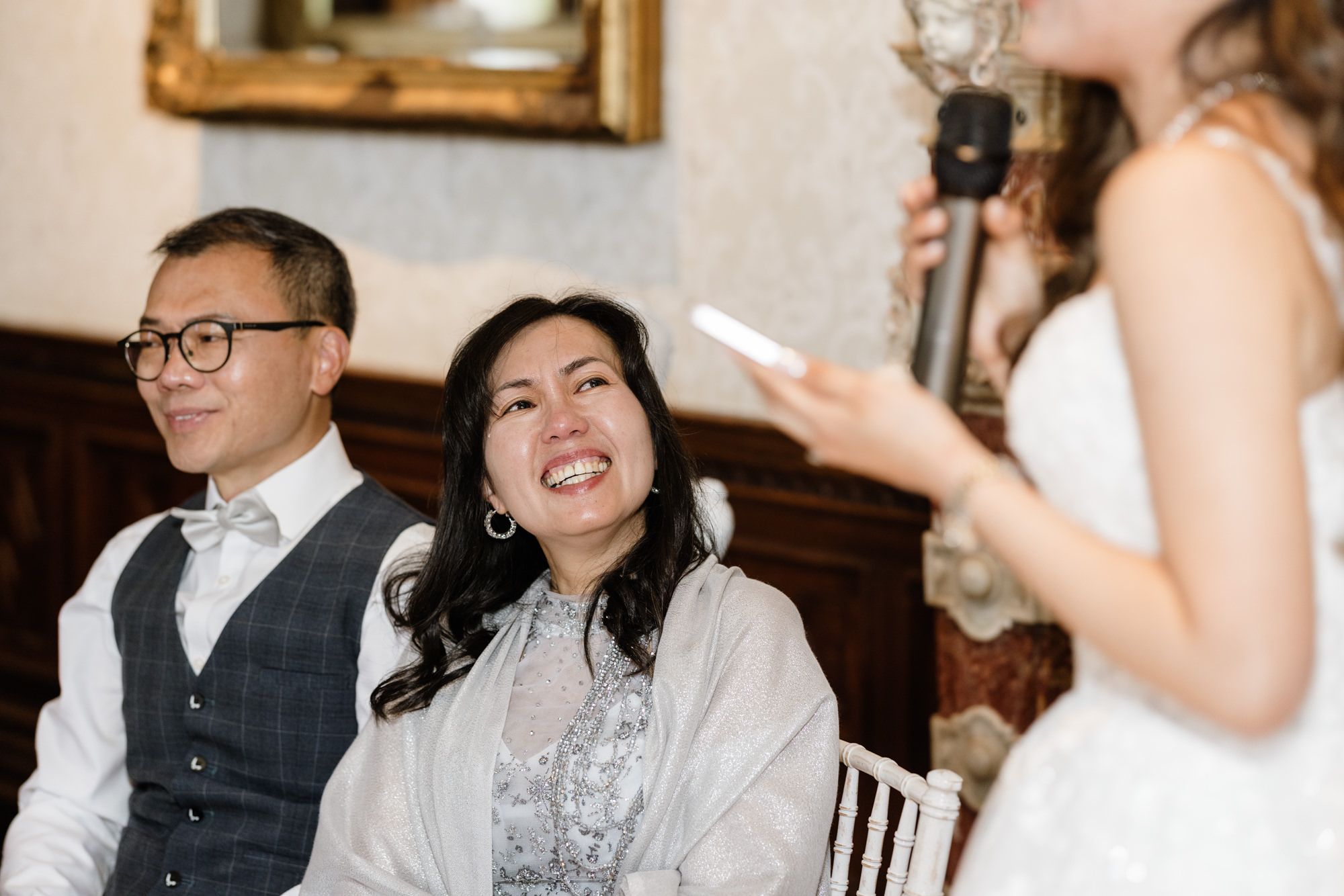 Couple smiling joyfully during a wedding speech at an elegant indoor reception venue.