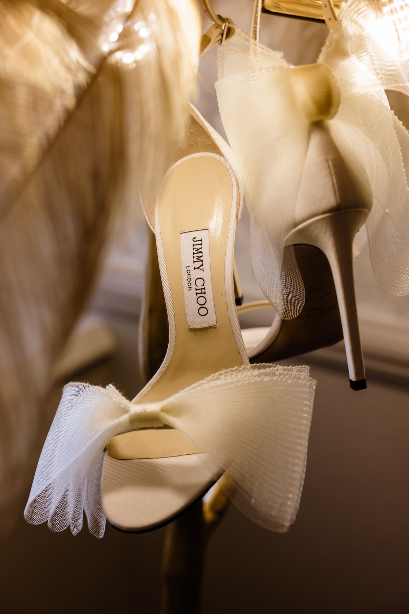 Elegant ivory Jimmy Choo high heel sandals with tulle bow detail displayed on a hanger for a bridal wedding look.