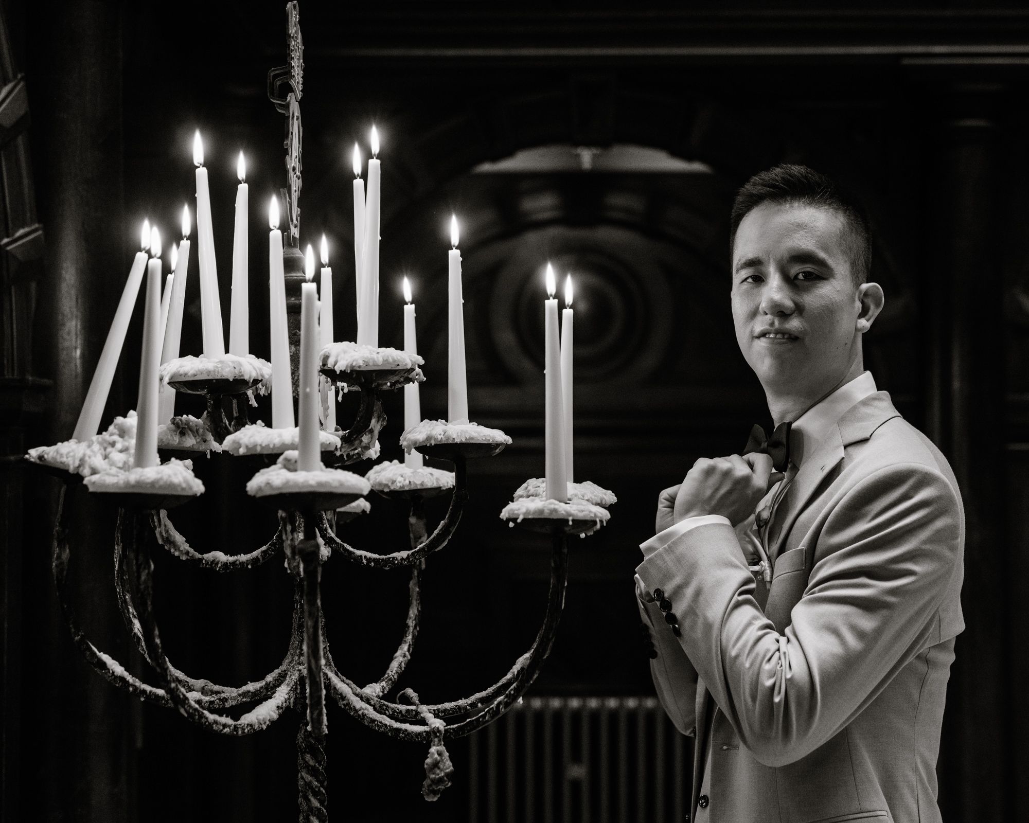 Black and white portrait of a man in a suit standing beside a lit candelabra with tall white candles.