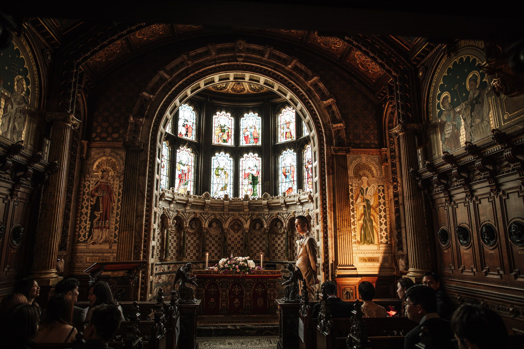 Ornate church interior with stunning stained glass window and intricate carved wooden altar during a wedding ceremony.