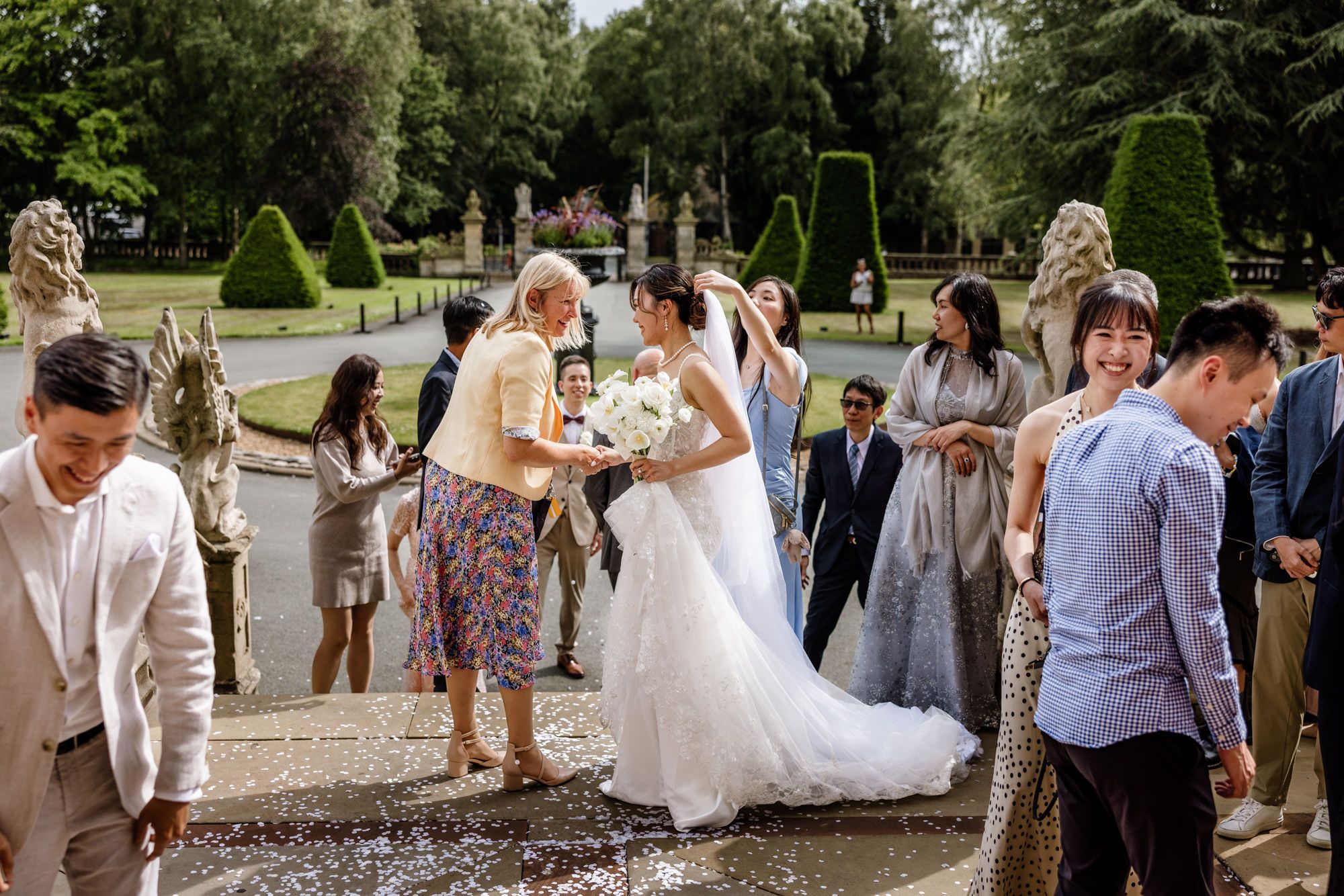 Bride in white gown walks through garden wedding ceremony as guests celebrate with confetti at elegant outdoor venue.
