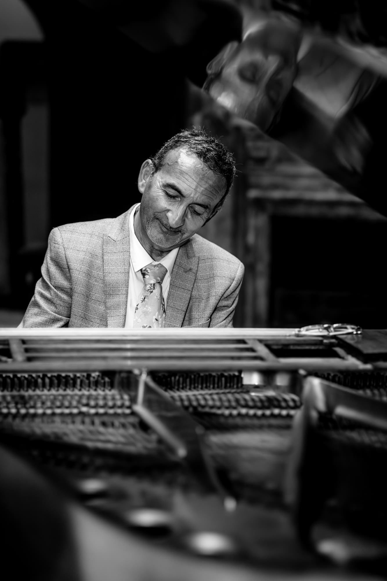 Black and white photo of a smiling man in a suit playing a grand piano on stage.