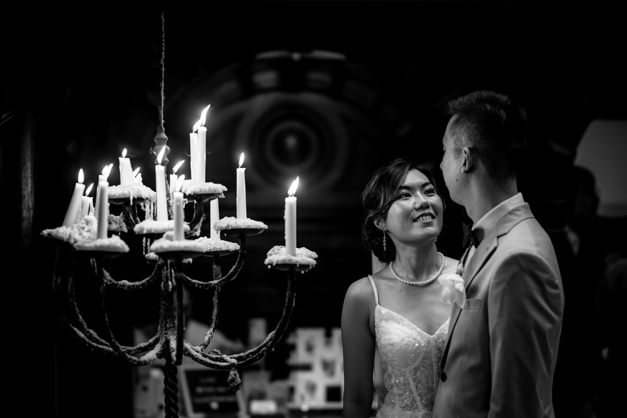 Black and white wedding photo of couple sharing a romantic moment beside a lit candelabra in elegant venue.
