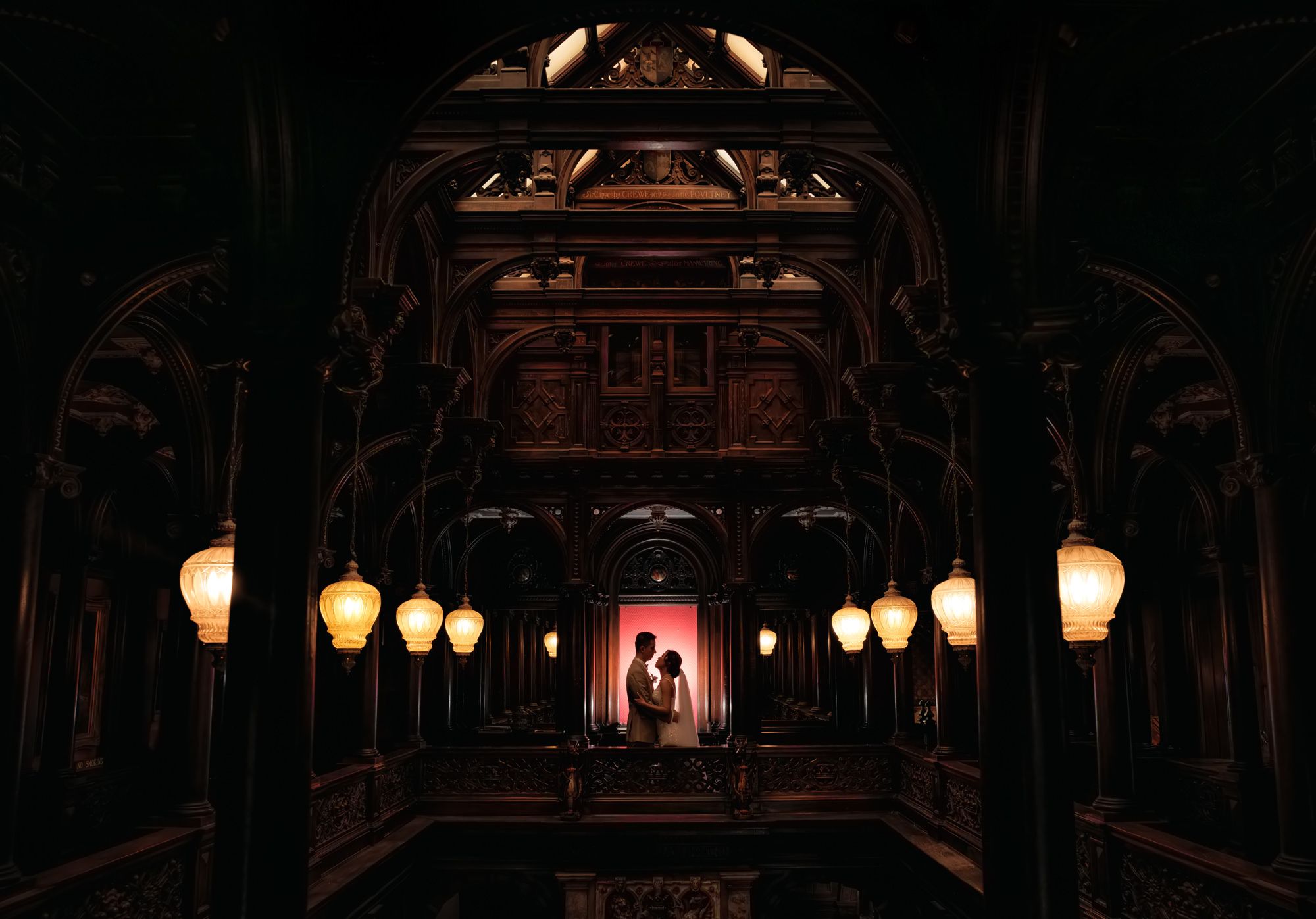 Couple silhouetted in ornate dark venue with glowing lanterns during romantic wedding portrait session.