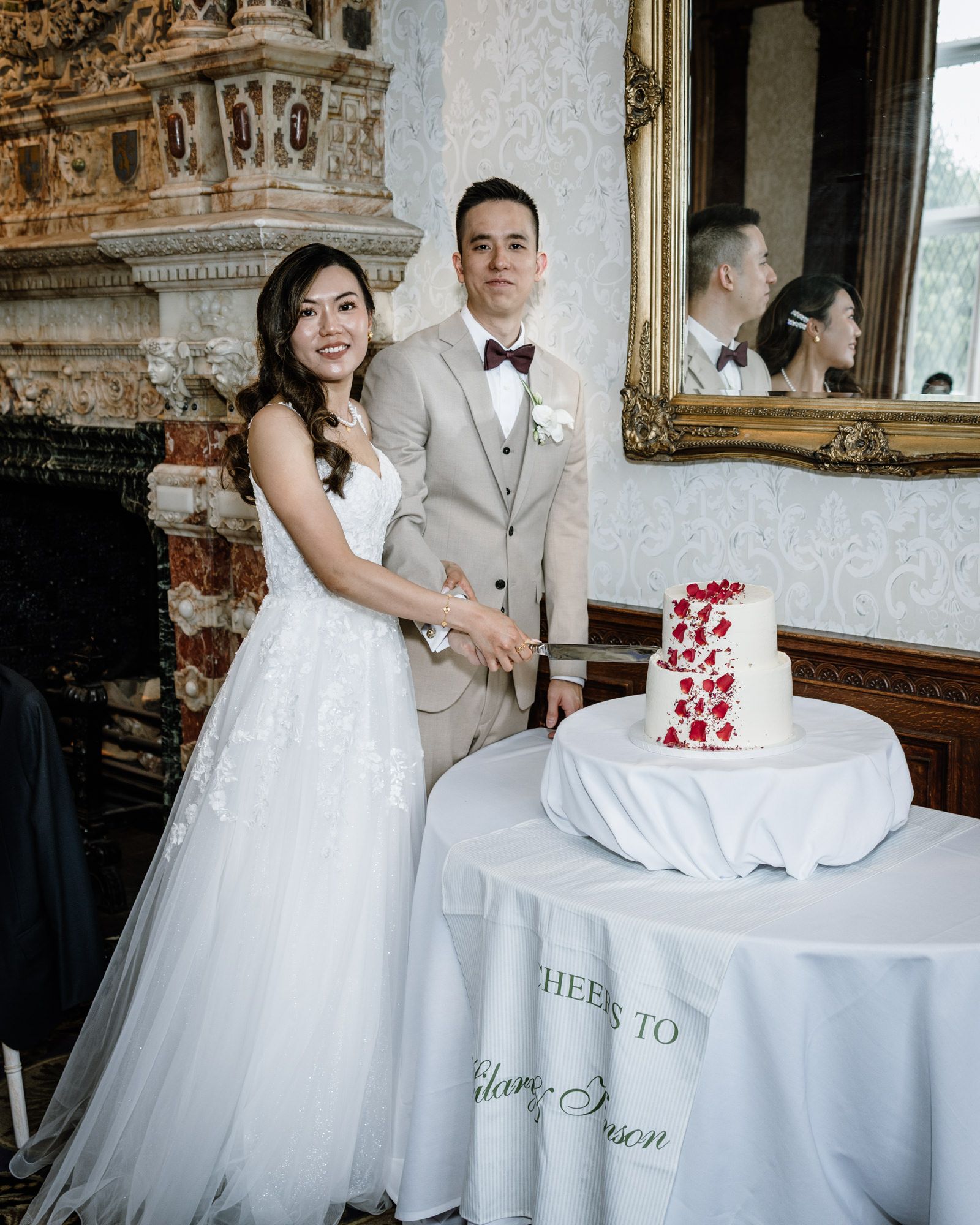 Bride and groom cutting their white wedding cake adorned with red roses at an elegant venue reception.