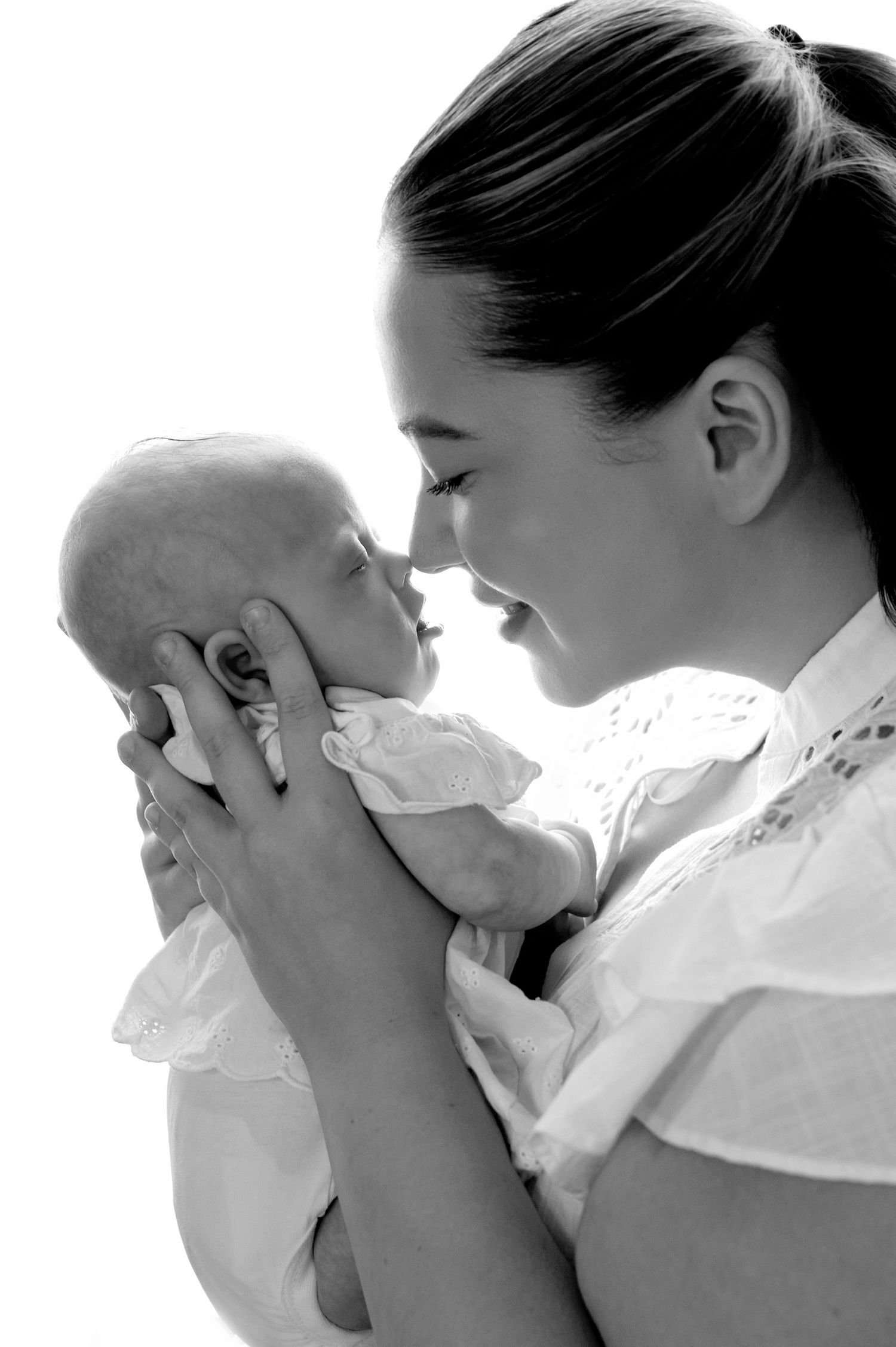 Black and white photo of a smiling mother holding her newborn baby face-to-face in a tender moment.
