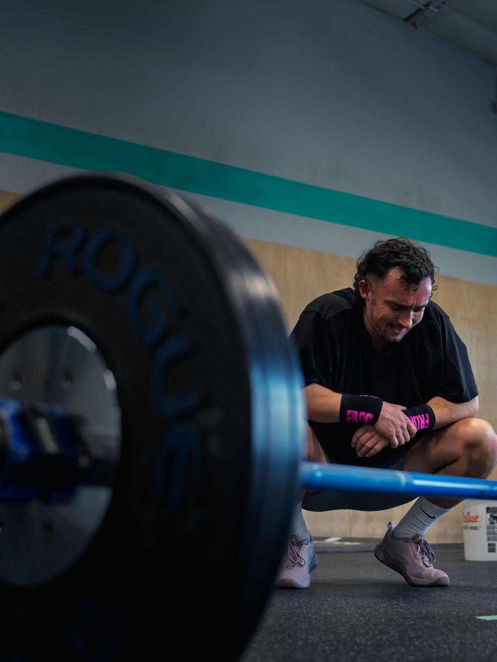 CrossFit athlete crouches to rest behind a loaded barbell at CrossFit Mojo in Madison, WI, head down and gathering himself between rounds.