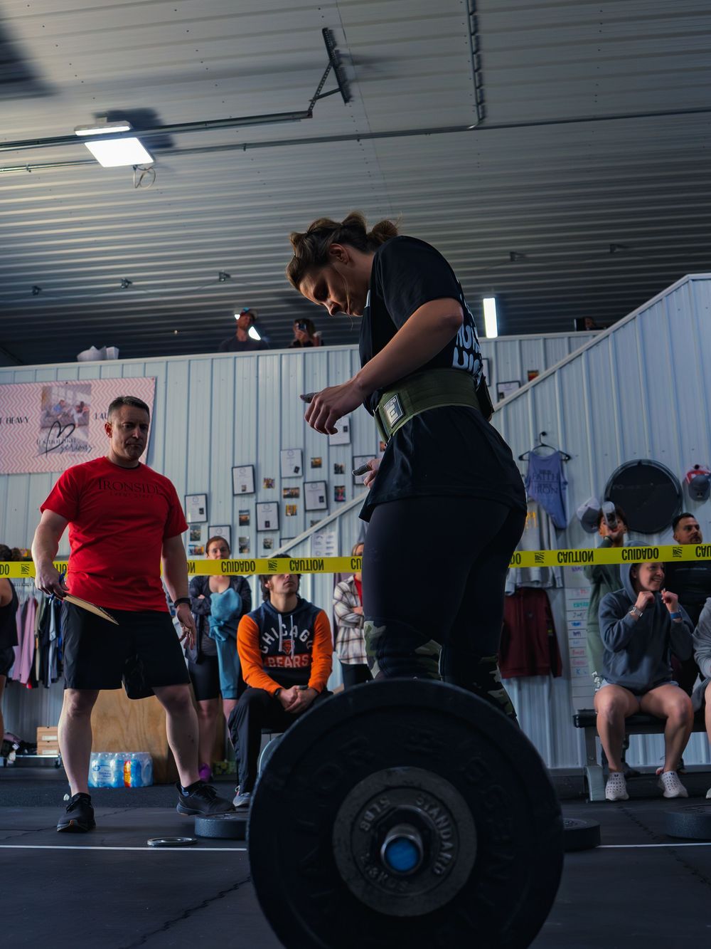 CrossFit athlete in a lifting belt sets her grips and stares down a loaded barbell before a lift at a competition in Janesville, WI.